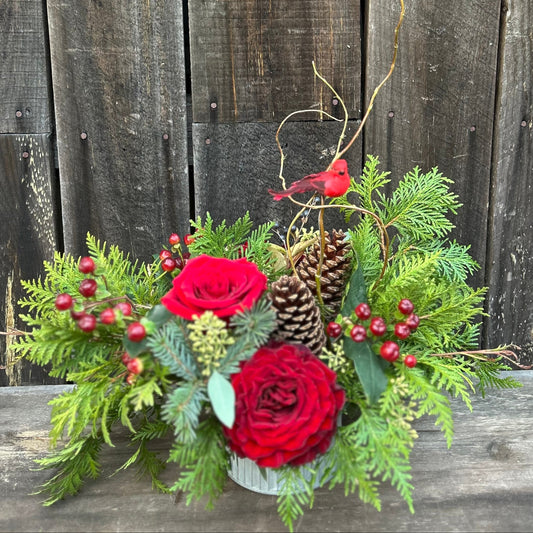 Floral arrangement with red roses, greenery, pinecones, and berries 