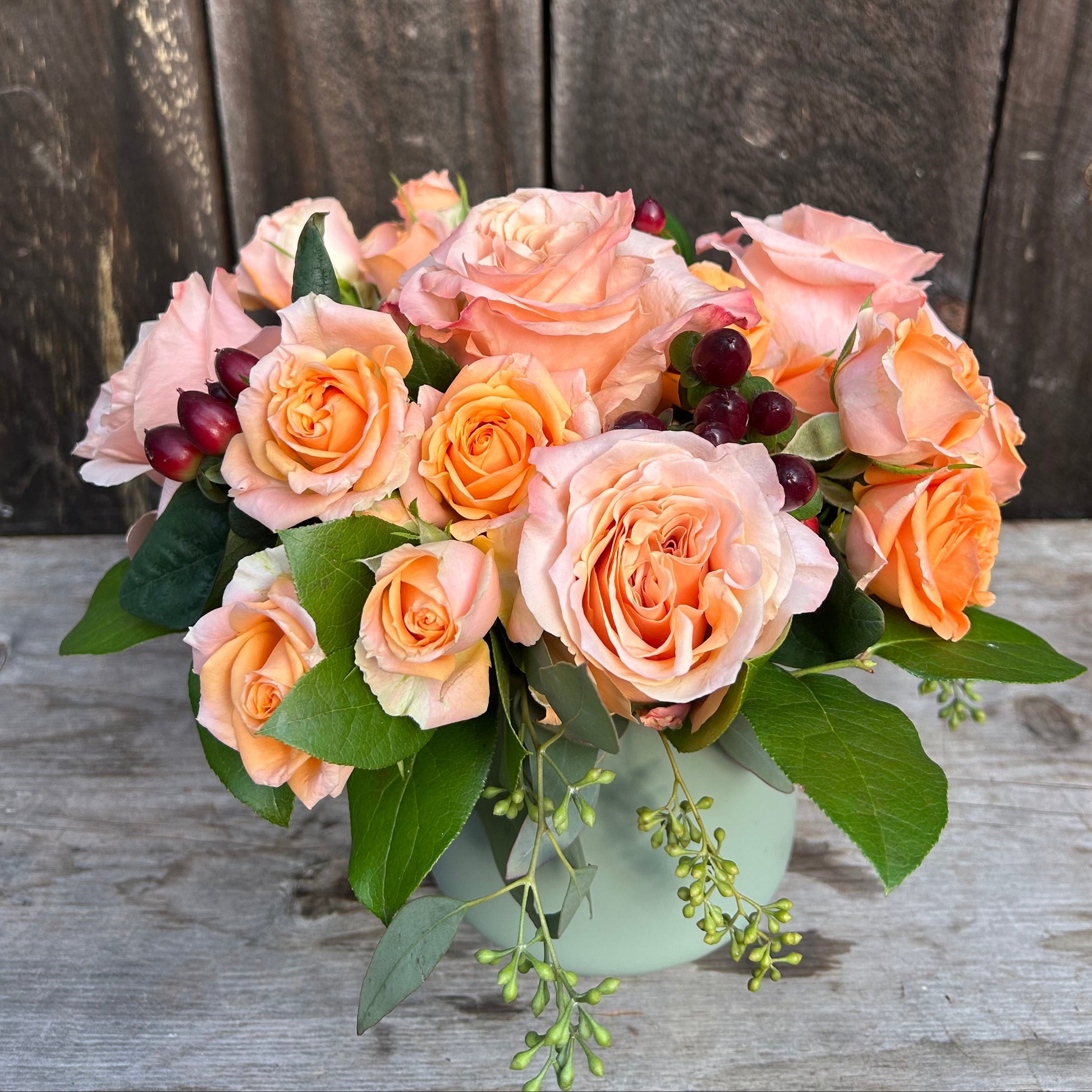 Bouquet of peach-colored roses with greenery on a wooden surface and background.